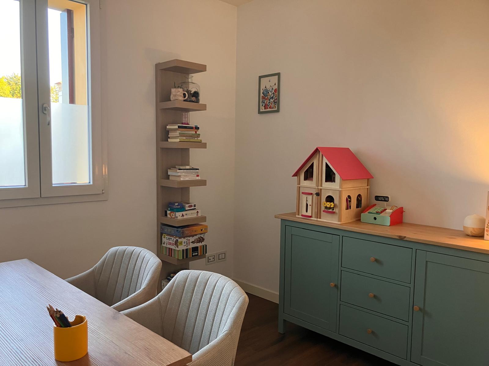Un angolo dello studio: la libreria con i libri e i giochi, la credenza e la casa delle bambole